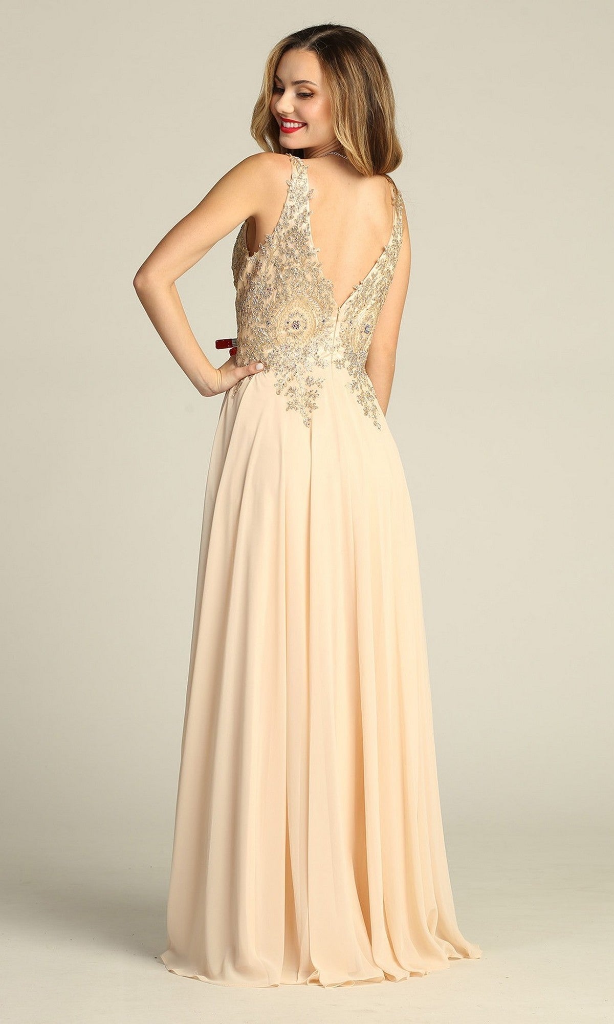 A woman stands smiling in the Chicas DM4006 long formal dress, which features a floor-length beige chiffon A-line skirt, silver embellishments, and an open back as she faces away from the camera.